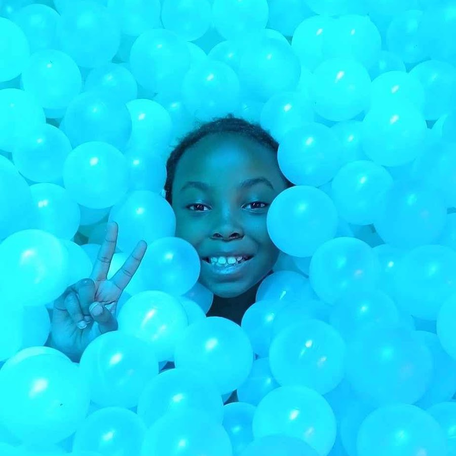 Rin smiling in a pool of bright blue balls, from her YouTube channel